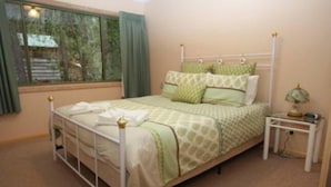 Una cama individual con estructura metálica, una mesita de noche con lámpara y una ventana con cortinas.