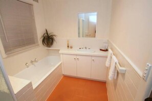 Une salle de bain avec une baignoire, des meubles blancs, un lavabo, un miroir et une plante en pot.