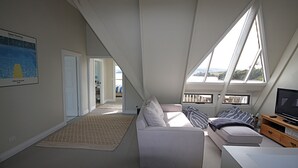 A modern loft bedroom with a large window, a sofa, a TV, and a bookshelf.