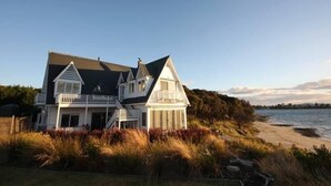 A two-story house with a balcony, located near a beach with grassy dunes.