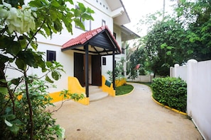 Enter a serene oasis with a covered entrance area, surrounded by lush greenery and trees.