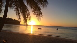 A beach at sunset with calm waters, a boat, and a palm tree. - Amazing, Luxury condominium on the 18 hole of Dye Fore  Golf Course (La Romana)