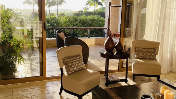 A spacious room with a large sliding glass door leading to a balcony, a ceiling fan, and a table with candles and snacks. - Amazing, Luxury condominium on the 18 hole of Dye Fore  Golf Course (La Romana)