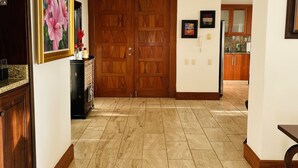 A hallway with a wooden door, a framed painting, and a kitchen visible in the background. - Amazing, Luxury condominium on the 18 hole of Dye Fore  Golf Course (La Romana)