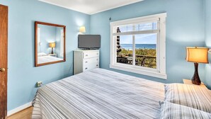 Une chambre à coucher comprenant un lit, une commode, un téléviseur, une fenêtre donnant sur un beau paysage et une lampe.