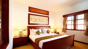 A neatly made bed with a wooden headboard, two bedside tables with lamps, a large framed artwork above the bed, and a window with curtains. - Sanur, Elegant 2 Bed Villa
 (Sanur)