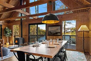 Een houten interieur met een eettafel voor vier personen, een open haard en grote ramen met uitzicht op het omliggende landschap.