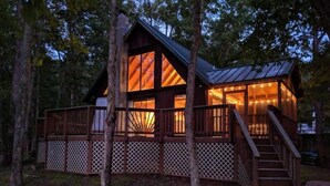 A cabin with a large window, wooden deck, and a staircase leading to the entrance.