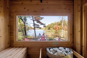 A wooden cabin with a large window overlooking a lake and trees. - Cozy Cabin | Lakefront, Hot Tub, Outdoor Sauna (Harpers Ferry)