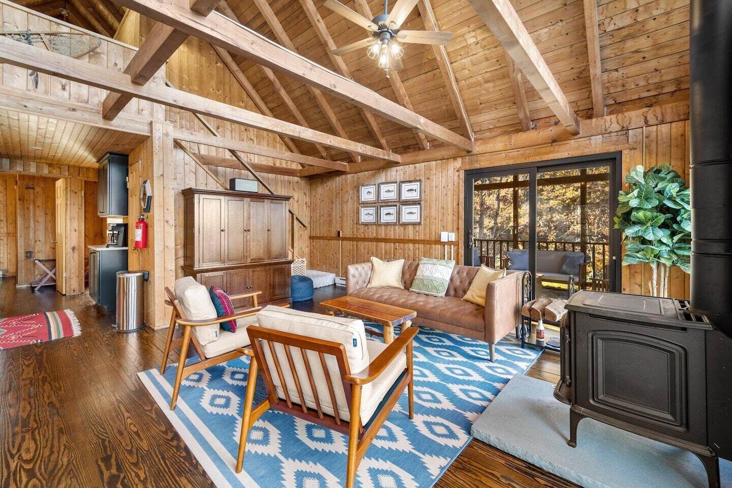A rustic cabin interior with a wooden ceiling, a fireplace, a sofa, a coffee table, and a dining table.
