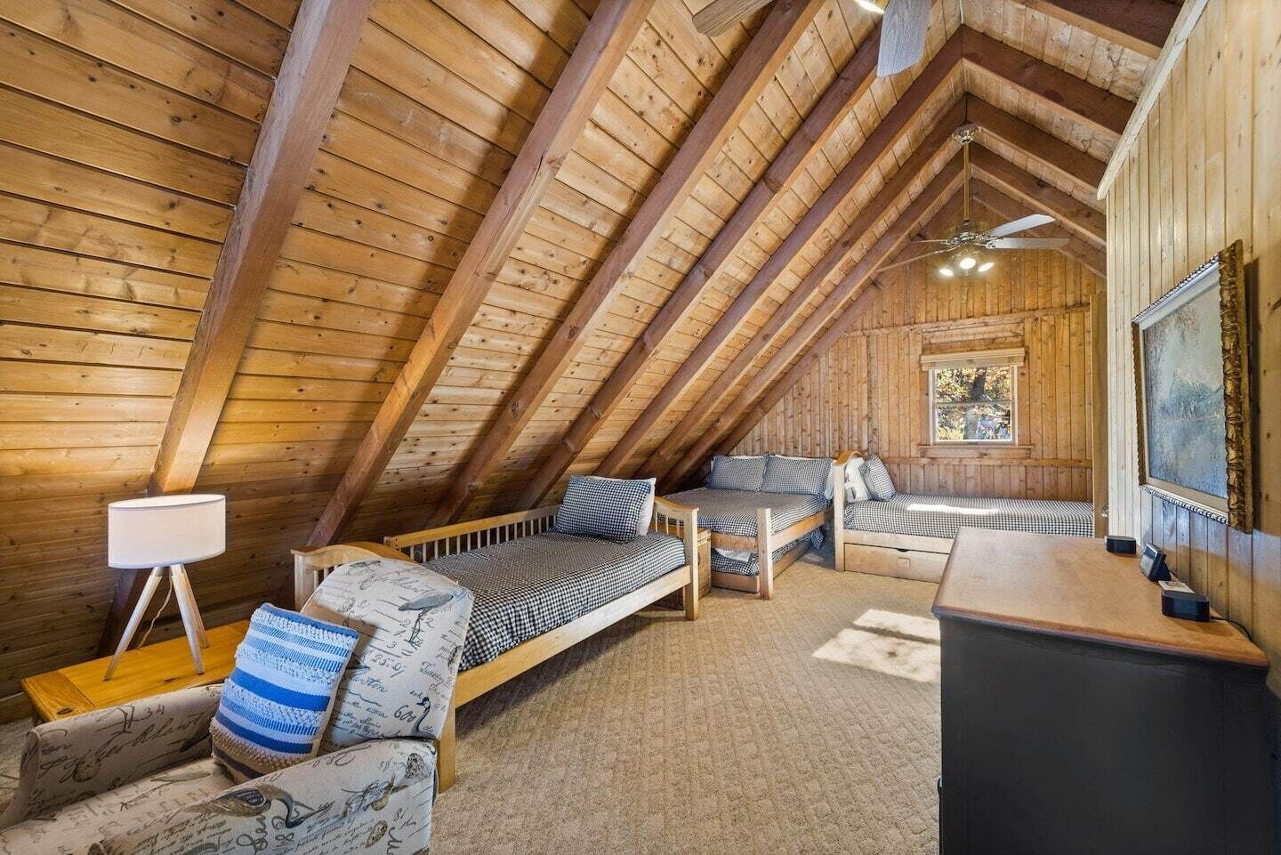 Une chambre mansardée chaleureuse avec des poutres en bois, un lit, une chaise, un bureau et une fenêtre.