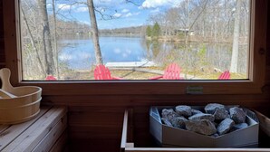 A cabin with a large window overlooking a lake, a red Adirondack chair, and a box of firewood.