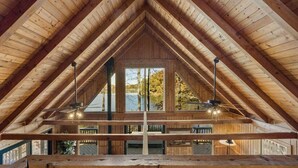 An attic room with a wooden sloped ceiling, large windows, and a wooden deck.