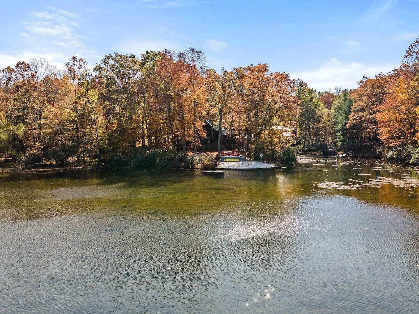 Un cadre paisible au bord d’un lac, avec le feuillage automnal, un quai et un petit bâtiment, probablement une cabane ou un chalet.