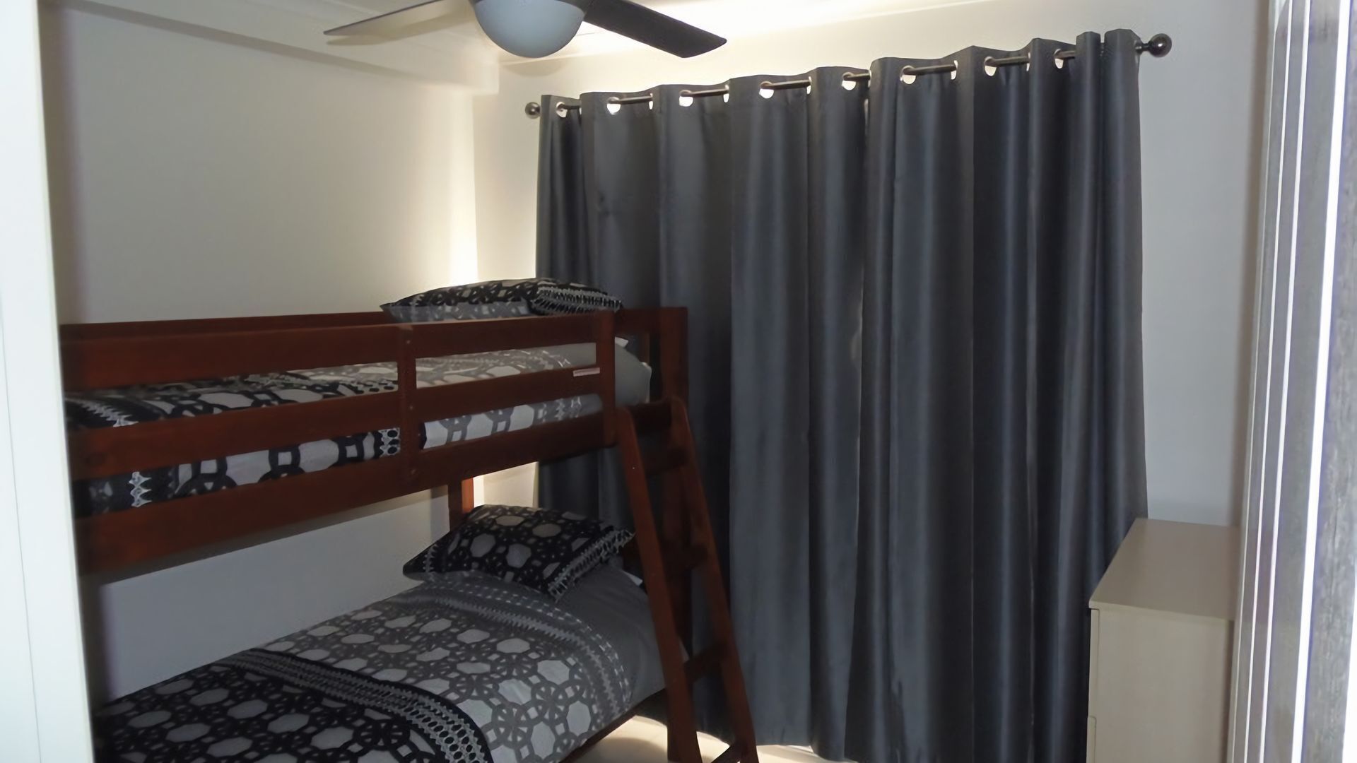 A bunk bed room with a ceiling fan, grey curtains, and a white wall.