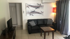 Un salón con un sofá de cuero negro, una mesa de centro de madera, un televisor de pantalla plana sobre un mueble y arte abstracto en la pared.