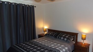 Un dormitorio con una cama, dos lámparas de noche, una cortina oscura y una colcha estampada.