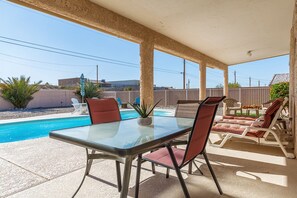 A covered patio with a glass table and chairs, a pool, and lounge chairs. - Spacious, Super Clean, Ping Pong & Alexa music!! (Lake Havasu)