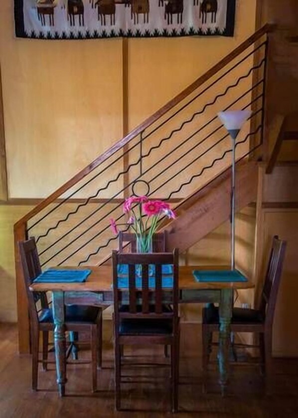 Un coin repas avec une table et des chaises en bois, un vase de fleurs et un escalier doté d’une rampe.