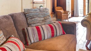A cozy living room with a brown sofa, striped and woven throw pillows, a wicker chair, and a view of the outdoors through a sliding glass door. - Howards Hill bed & breakfast (cape schanck)