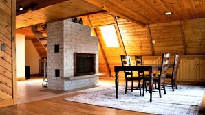 A cozy attic room with a stone fireplace, wooden ceiling beams, and a dining table with chairs. - Great Sacandaga Lakefront Home with 100 feet of deep water access (Hadley)