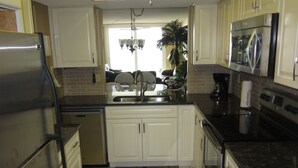 A kitchen with white cabinets, a stainless steel refrigerator, a dishwasher, a stove, and a microwave. - Direct Beach Front - Updated Unit - Last Minute July Special! (Indian Shores)
