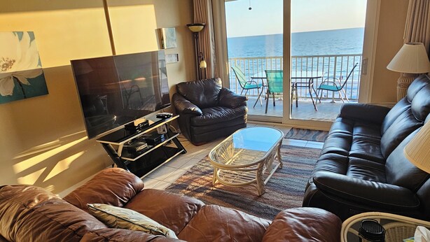 A living room with a sofa, a glass coffee table, and a TV. There is a balcony with a view of the sea. - Direct Beach Front - Updated Unit - Last Minute July Special! (Indian Shores)