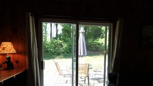 Ein Zimmer mit Holzeinrichtung, einer Glasschiebetür, die auf eine Terrasss führt, einem Tisch mit Stühlen und einer Bank.
