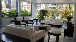 A modern living room with a sofa, chairs, and a coffee table. Large windows provide a view of the city. - 🌺RIVIERA APARTMENT WITH SEA VIEW (send message before) (Bertioga)