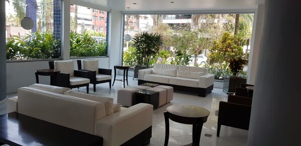 A modern living room with a sofa, chairs, and a coffee table. Large windows provide a view of the city. - 🌺RIVIERA APARTMENT WITH SEA VIEW (send message before) (Bertioga)