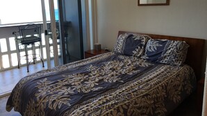 A bedroom with a bed, a nightstand, a chair, and a sliding glass door leading to an outdoor area. - Cozy Beach front condo in Makaha (Waianae)