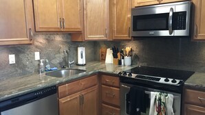 A kitchen with wooden cabinets, a stainless steel microwave, a stove, and a dishwasher. - Cozy Beach front condo in Makaha (Waianae)
