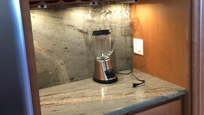 A kitchen with a blender on the counter, wooden cabinets, and a wine rack above. - Cozy Beach front condo in Makaha (Waianae)