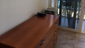 A wooden dresser with drawers, a flat-screen TV mounted on the wall, and a sliding glass door leading to a balcony with a view of the ocean. - Cozy Beach front condo in Makaha (Waianae)