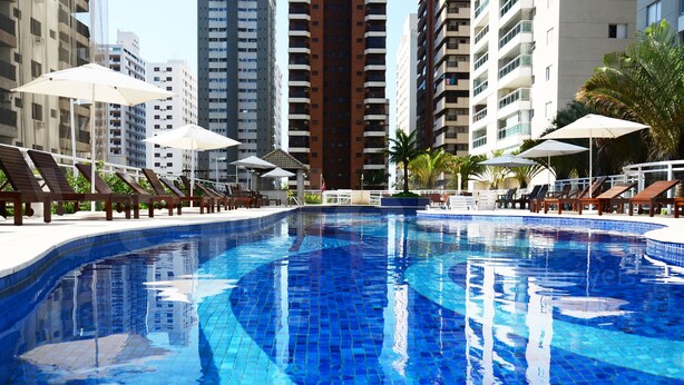 Ein Swimmingpool mit Liegestühlen und Sonnenschirmen, umgeben von hohen Wohngebäuden.