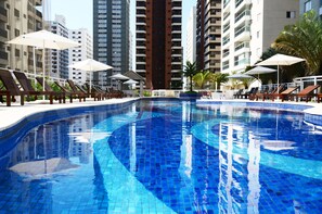 Une piscine entourée d’immeubles résidentiels imposants, avec des chaises longues et des parasols.