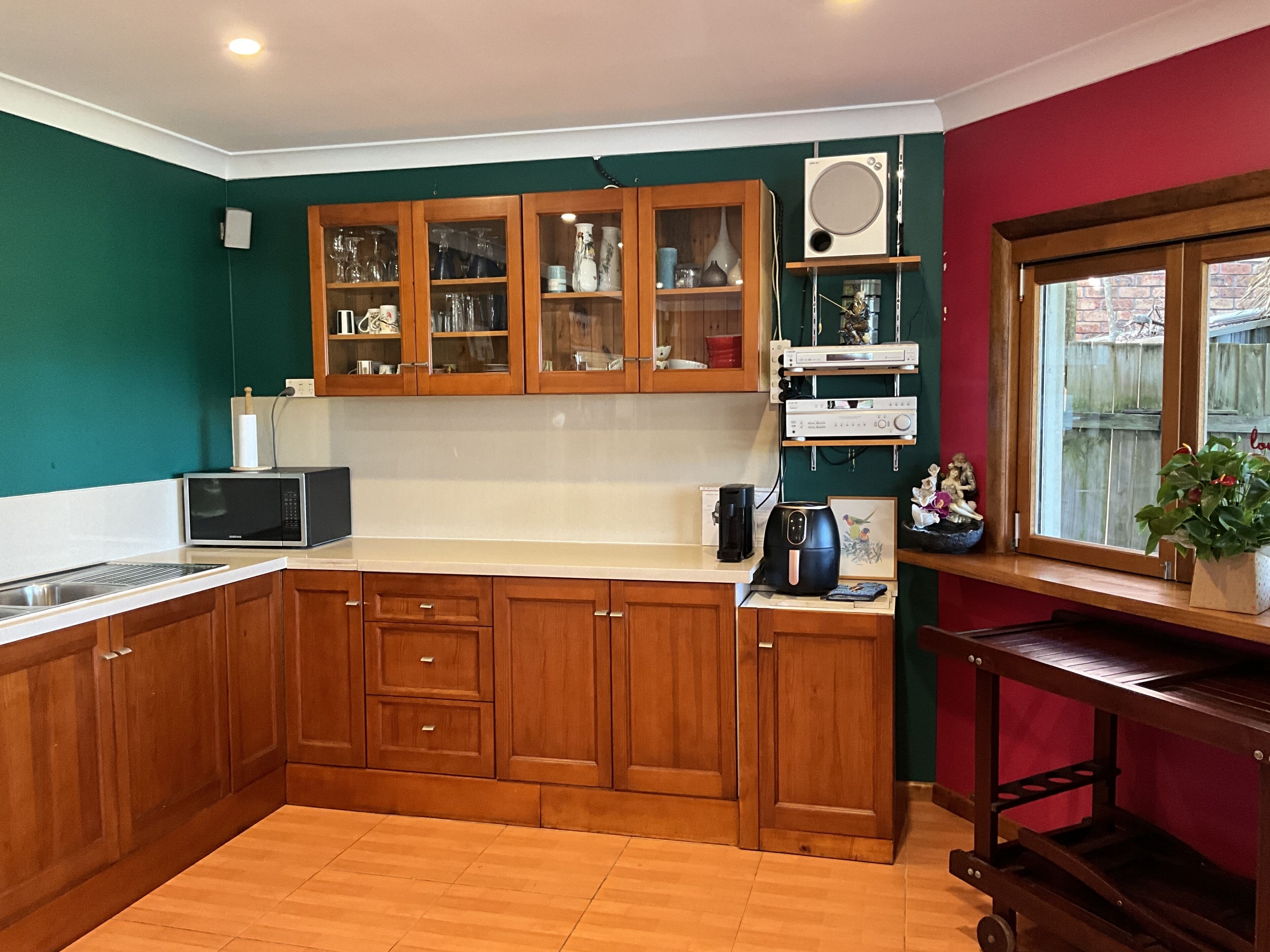 A kitchen with wooden cabinets, a microwave, a coffee maker, and a window with a view of a fence.