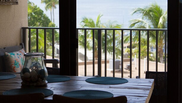A wooden table with a glass jar and decorative pillows, overlooking a beach with palm trees and the ocean. - Stunning Ocean View/Sunsets, A true "Gem by the Sea" great for relaxation & fun (Key Largo)