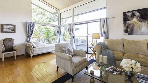 Uma sala de estar ampla com piso de madeira, um sofá, uma poltrona e uma mesa de centro de vidro com velas e flores.