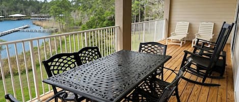 A covered outdoor deck with a table and chairs, overlooking a lake and dock.