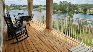 A wooden deck with a table and chairs, overlooking a lake with boats and houses.