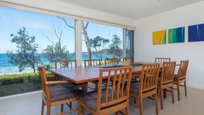 A dining area with a view of the sea, wooden chairs, a table, and three paintings on the wall. - Beachfront Duplex on Denhams (Denhams Beach)