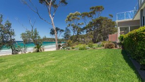 A coastal property with a well-maintained lawn, a variety of trees, and a view of the ocean. - Beachfront Duplex on Denhams (Denhams Beach)