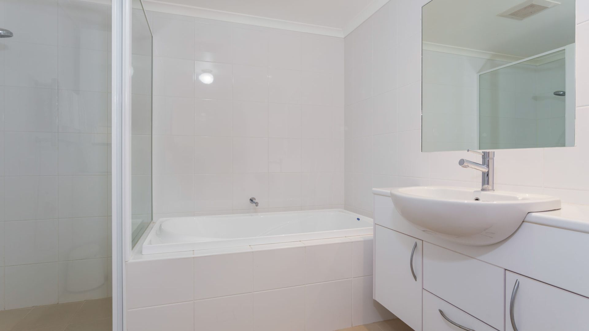 A modern bathroom with a glass-enclosed shower, a white bathtub, and a white sink with a mirror above it.