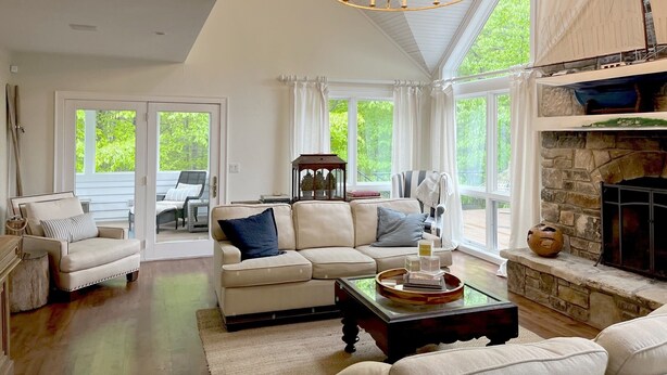 A spacious living room with a high ceiling, a stone fireplace, and large windows offering a view of greenery outside. - Private, Luxury Family Retreat 3min  to downtown Ephraim & Sister Bay, Door Co (Sister Bay)