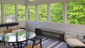 A sunroom with a glass table surrounded by chairs, a bench, and a sofa. Large windows provide a view of a green forest. - Private, Luxury Family Retreat 3min  to downtown Ephraim & Sister Bay, Door Co (Sister Bay)