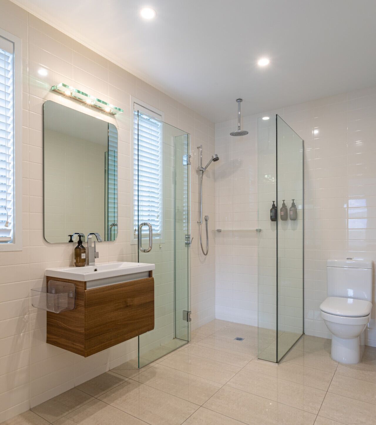 Une salle de bain moderne avec une douche à parois de verre, des toilettes blanches et un meuble-lavabo doté d’un miroir et d’un distributeur de savon.
