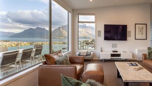 Een moderne woonkamer met een groot raam met uitzicht op de bergen, een flatscreen-tv en een zithoek met een bijzettafeltje.