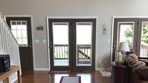Amplia sala de estar con pisos de madera, un tapete central, un banco y un sofá. Dos puertas dobles dan al exterior, cada una con un pequeño ventanal.