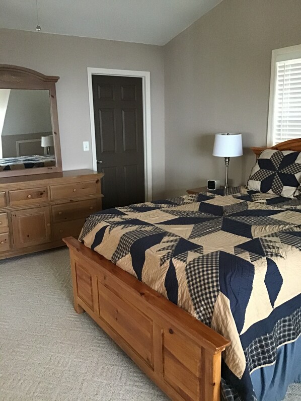 A bedroom with a wooden bed, a dresser, a mirror, a door, a lamp, and a window with blinds.